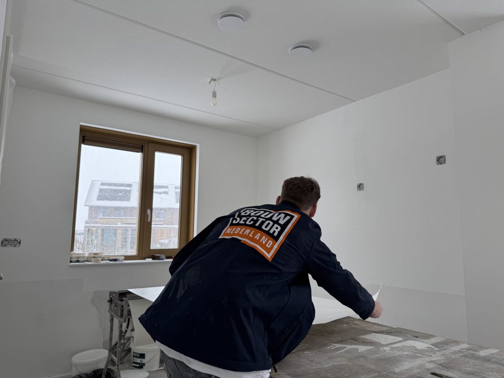 Vakman van Bouwsector Nederland snijdt een baan behang op maat aan de plaktafel