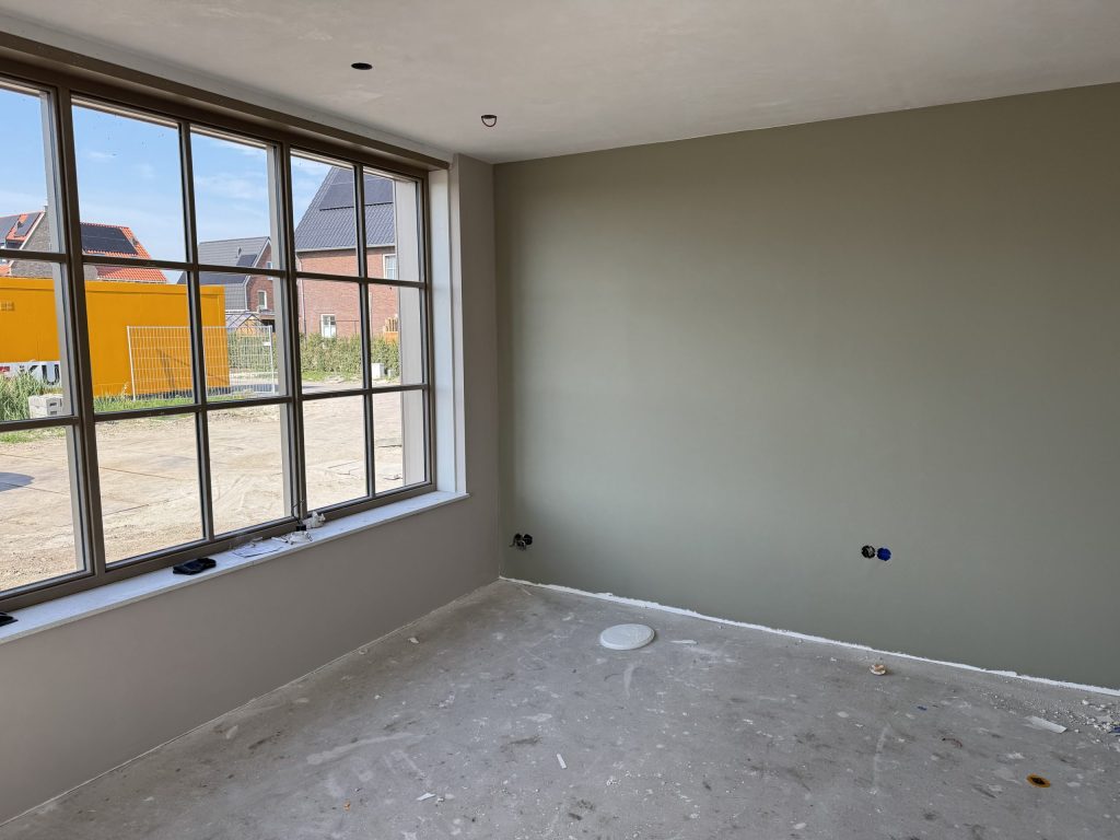 Kamer met een egaal gesausde wand in grijsgroen naast een groot raam