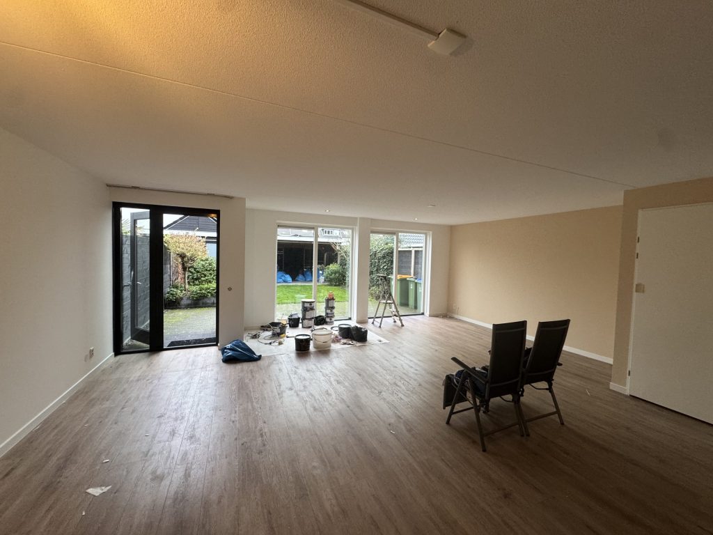 Lege woonkamer met lichte wanden, tuindeuren en schildersmateriaal op de vloer