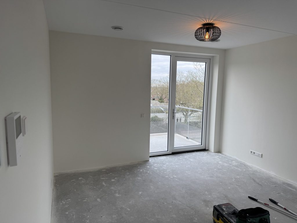 Lege kamer met gladde witte wanden en een balkondeur, kort na de oplevering