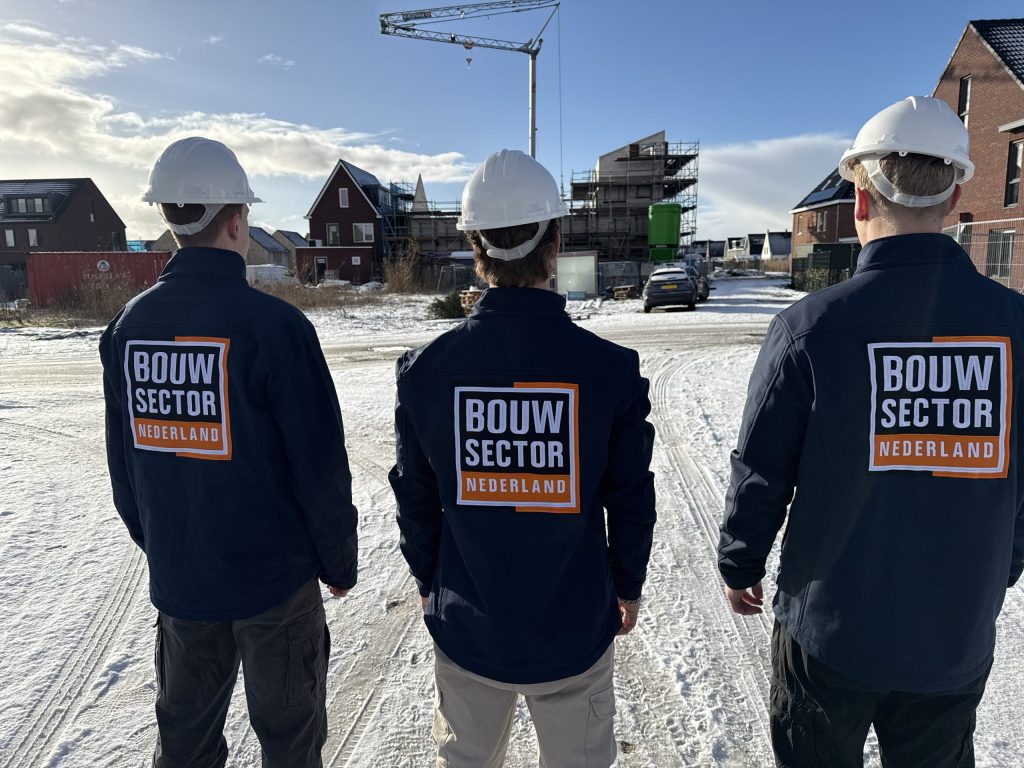 Drie vakmensen van Bouwsector Nederland met witte helm bij woningen in aanbouw in de sneeuw